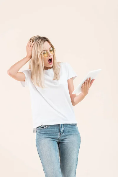 Femme élégante choquée dans les lunettes de vue regardant tablette numérique isolé sur beige — Photo de stock