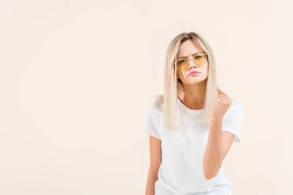 Mujer joven enojada en gafas de sol agitando el puño y mirando a la cámara aislada en beige - foto de stock