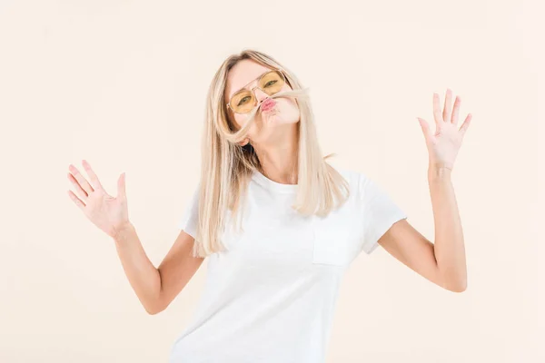 Young blonde woman in sunglasses having fun with hair and looking at camera isolated on beige — Stock Photo