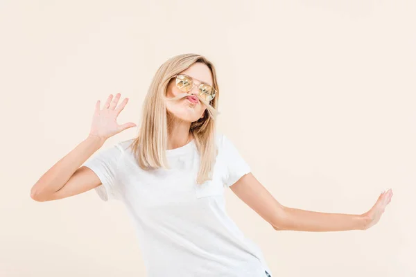 Joven rubia en gafas de sol divirtiéndose con el pelo aislado en beige - foto de stock