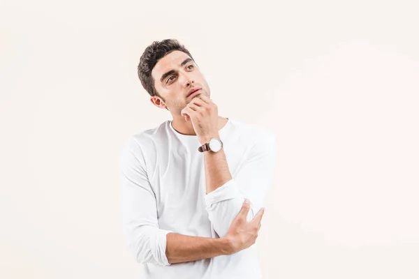 Thoughtful young man with hand on chin looking away isolated on beige — Stock Photo