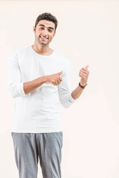 Handsome young man pointing at copy space and smiling at camera isolated on beige — Stock Photo