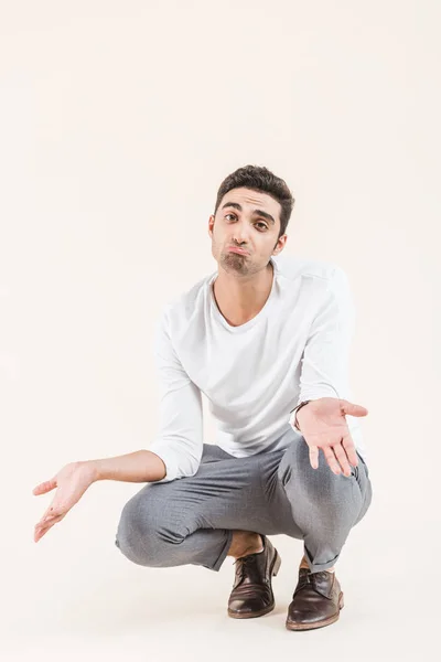 Disappointed young man crouching and looking at camera isolated on beige — Stock Photo