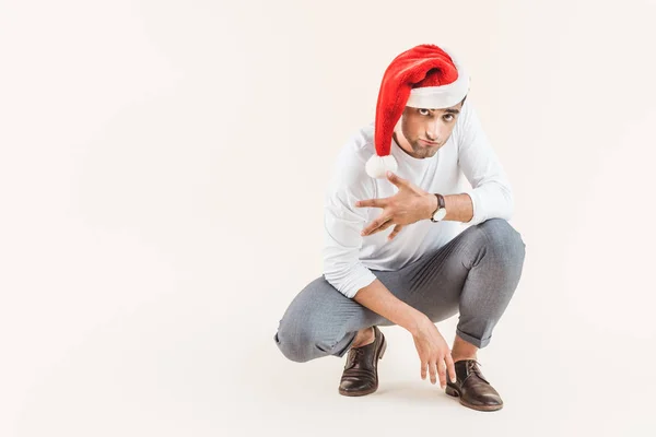 Handsome young man in santa hat crouching and looking at camera isolated on beige — Stock Photo