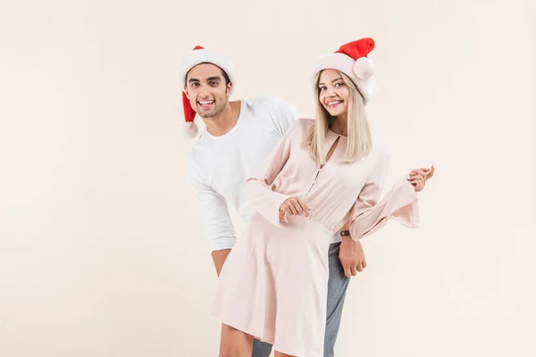 Bella felice giovane coppia in cappelli di Babbo Natale sorridente alla fotocamera isolata sul beige — Foto stock