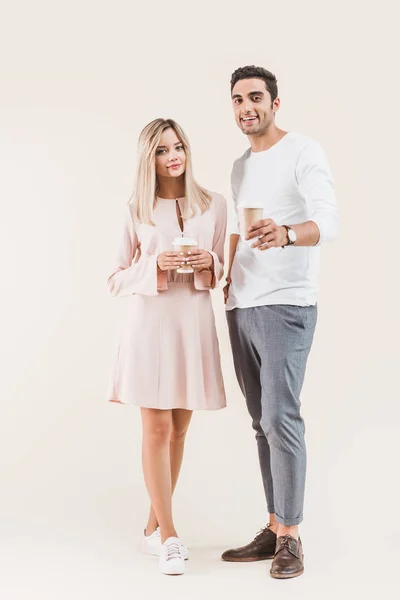 Giovane coppia che tiene tazze di carta e sorride alla fotocamera isolata sul beige — Foto stock