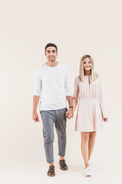 Glückliches junges Paar hält Händchen und lächelt in die Kamera isoliert auf beige — Stockfoto