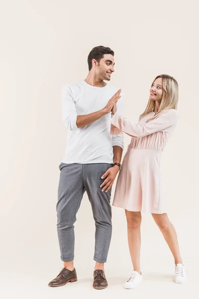 Feliz joven pareja dando alta cinco y sonriendo unos a otros aislados en beige - foto de stock