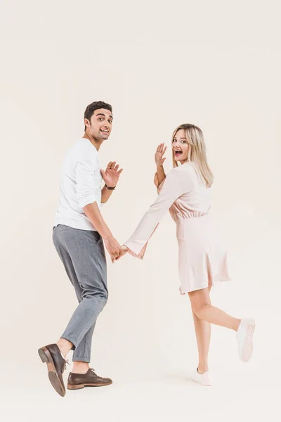 Jovem casal alegre de mãos dadas e sorrindo para a câmera isolada no bege — Fotografia de Stock