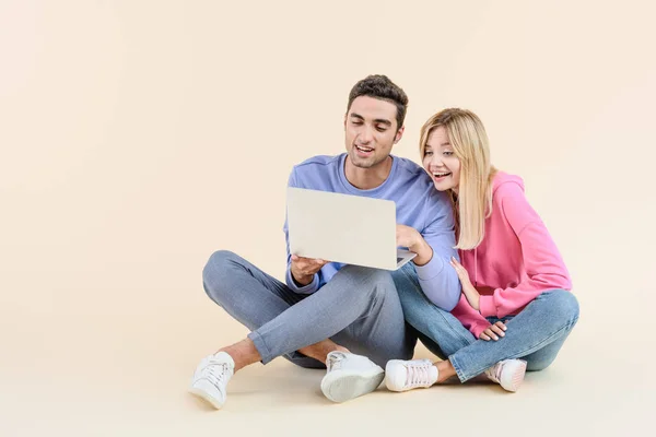 Happy young couple sitting together and using laptop isolated on beige — Stock Photo