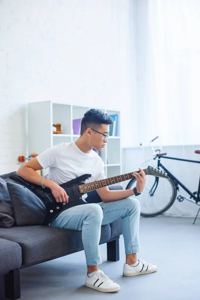 Красивый азиатский мужчина играет аккорд F на отключенной электрогитаре дома — стоковое фото