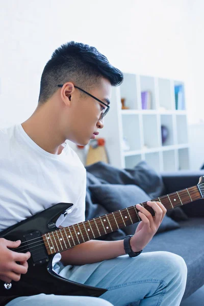 Guapo asiático hombre jugando eléctrico guitarra en casa - foto de stock