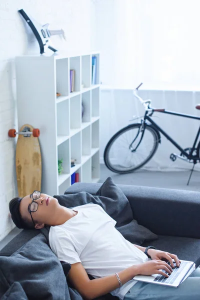 Alto angolo vista di bello asiatico uomo dormire e holding laptop su divano a casa — Foto stock