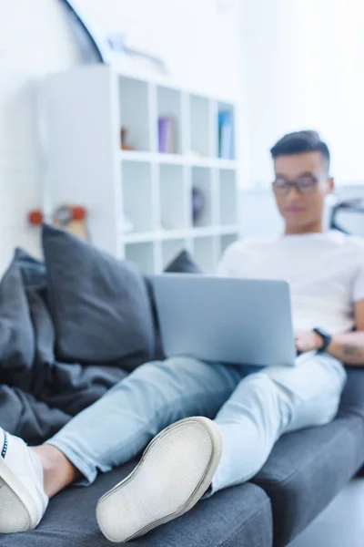 Selektiver Fokus eines hübschen asiatischen Mannes mit Laptop auf dem Sofa zu Hause — Stockfoto