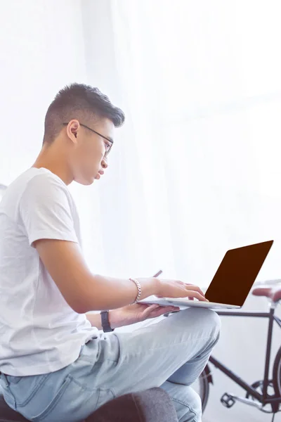 Side view of handsome asian man using laptop with blank screen on sofa at home — Stock Photo