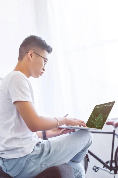 Side view of handsome asian man using laptop with online trade appliance on sofa at home — Stock Photo