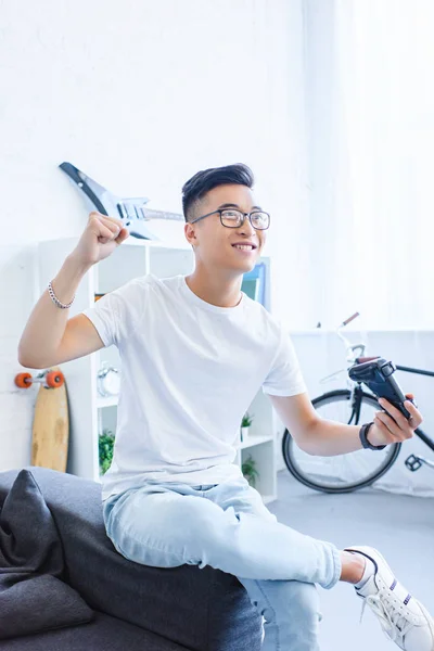 Felice bello asiatico uomo giocare video gioco e mostrando sì gesto a casa — Foto stock