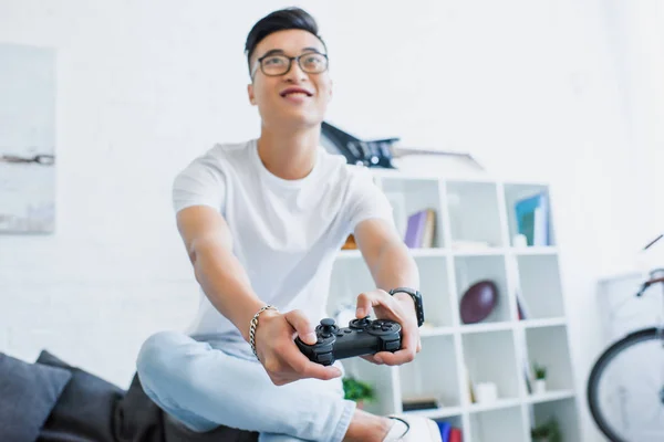 Selective focus of happy handsome asian man playing video game on sofa at home — Stock Photo