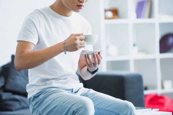 Обрізане зображення людини, що сидить на столі з чашкою кави вранці вдома — стокове фото