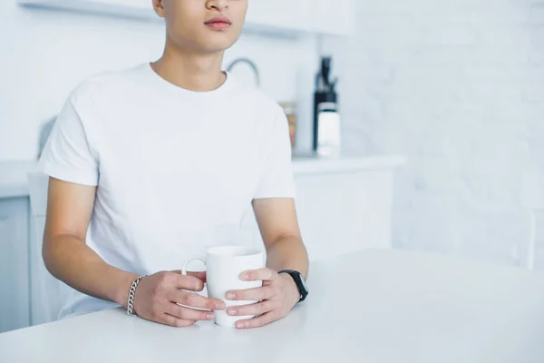 Обрезанный снимок молодого человека, держащего чашку чая за кухонным столом — стоковое фото