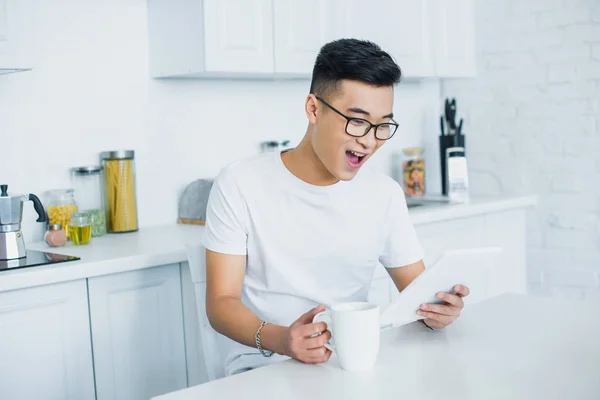 Joyeux jeune asiatique homme dans lunettes à l'aide de tablette numérique — Photo de stock