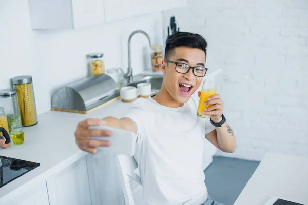 Счастливый молодой человек пьет сок и делает селфи со смартфоном — стоковое фото