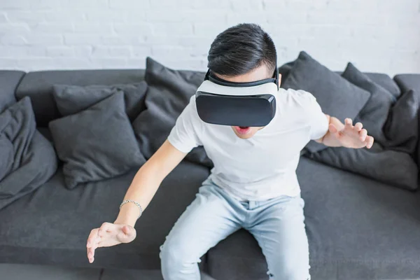Visão de alto ângulo de jovem emocional sentado no sofá e usando fone de ouvido realidade virtual — Fotografia de Stock