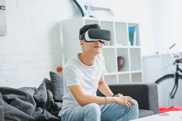 Sorrindo jovem asiático homem usando virtual realidade fone de ouvido em casa — Fotografia de Stock