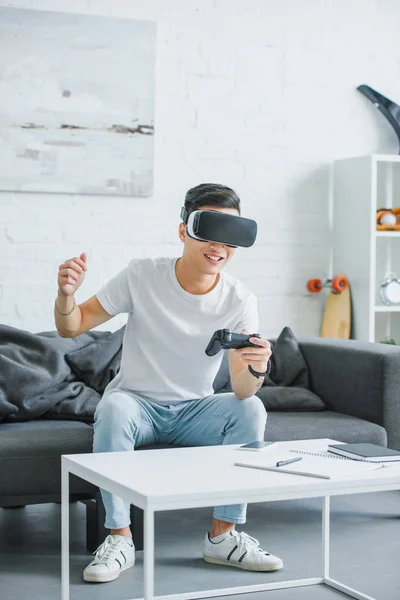 Збуджений молодий чоловік у гарнітурі віртуальної реальності грає з джойстиком вдома — стокове фото