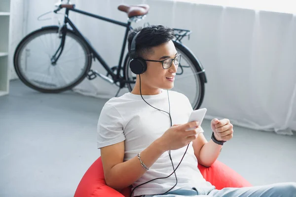 Blick aus der Vogelperspektive auf einen lächelnden jungen Mann, der sein Smartphone benutzt und über Kopfhörer Musik hört — Stockfoto