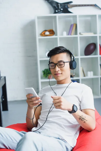 Handsome young asian man using smartphone and listening music in headphones — Stock Photo