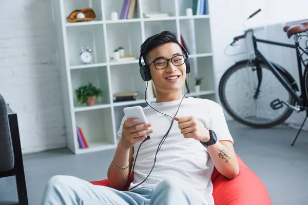 Jovem sorrindo usando smartphone e ouvindo música em fones de ouvido — Fotografia de Stock