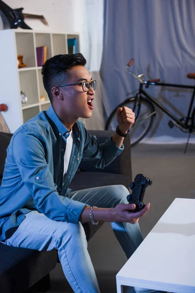 Excited young asian man playing video game with joystick and win at home — Stock Photo