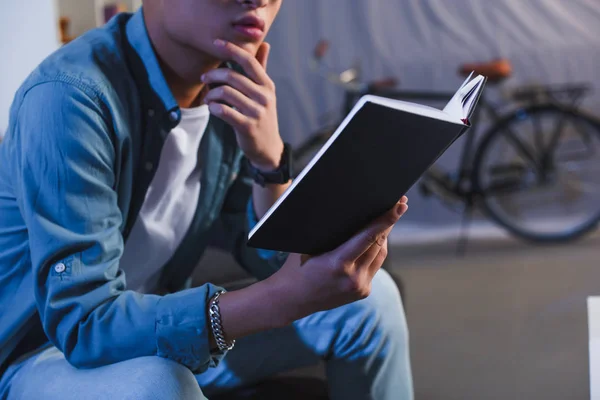 Plan recadré de réfléchi jeune homme lecture livre à la maison — Photo de stock