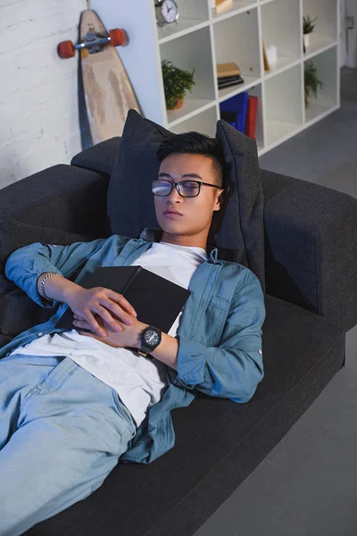 Високий кут зору молодого чоловіка в окулярах тримає книгу і спить на дивані — стокове фото