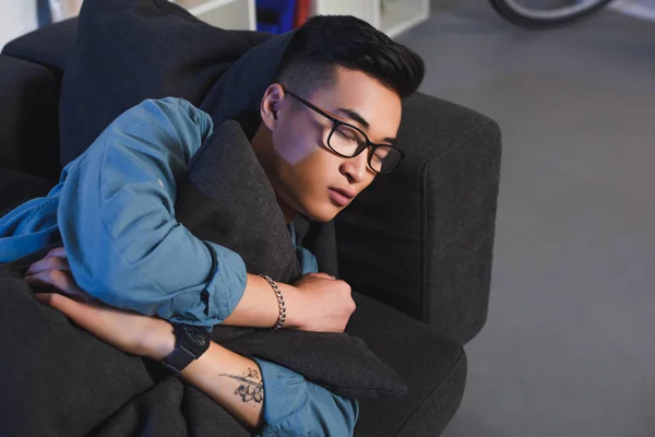 Alto ángulo vista de joven asiático hombre en gafas durmiendo en sofá en casa - foto de stock