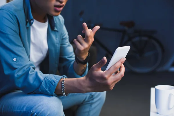 Cropped shot of young asian man using smartphone and giving middle finger — Stock Photo