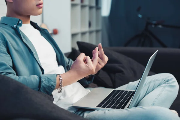 Cropped shot of young man sitting on couch and giving middle fingers to laptop — Stock Photo