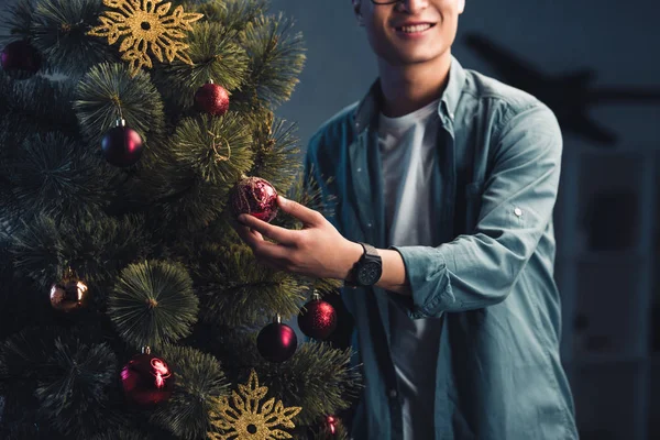 Schnappschuss eines lächelnden jungen Mannes, der zu Hause den Weihnachtsbaum schmückt — Stockfoto