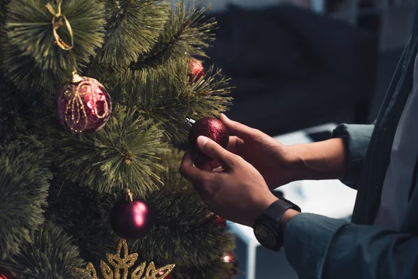Gros plan vue partielle du jeune homme décorant l'arbre de Noël à la maison — Photo de stock