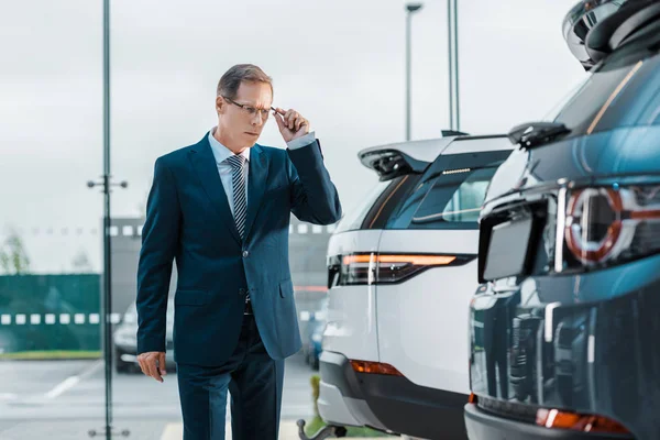 Businessman in eyeglasses choosing new car in dealership salon — Stock Photo