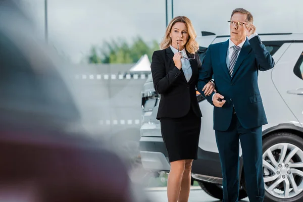 Pensive businessman and businesswoman choosing new automobile in showroom — Stock Photo