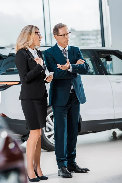Businessman and businesswoman with smartphone choosing new automobile in showroom — Stock Photo
