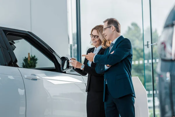 Businessman and smiling businesswoman choosing new automobile in showroom — Stock Photo
