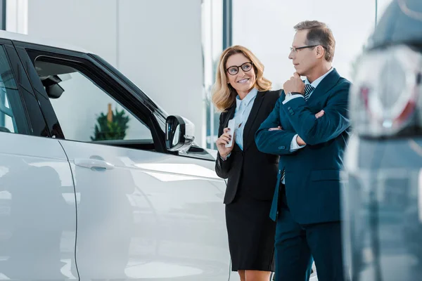 Couple d'affaires souriant à la recherche d'une nouvelle automobile dans le salon de concession — Photo de stock