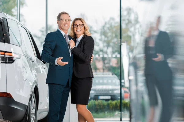 Sorrindo casal de negócios à procura de novo automóvel no salão de concessionárias — Fotografia de Stock