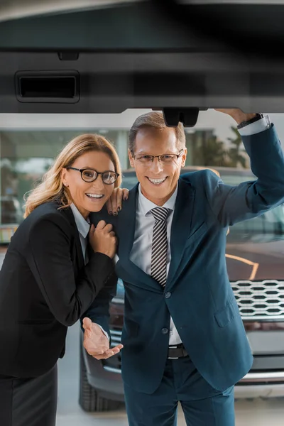 Smiling couple in formal wear looking at new car in dealership salon — Stock Photo