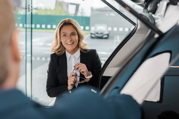 Частичный взгляд счастливой предпринимательницы и бизнесмена, стоящих у нового автомобиля в выставочном зале — стоковое фото
