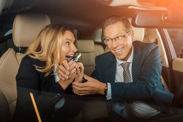 Glückliches Paar in formeller Kleidung mit Autoschlüssel sitzt im neuen Auto für eine Probefahrt — Stockfoto