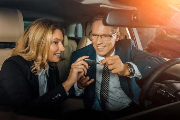 Pareja en desgaste formal con la llave del coche sentado en el coche nuevo para la prueba de conducción - foto de stock